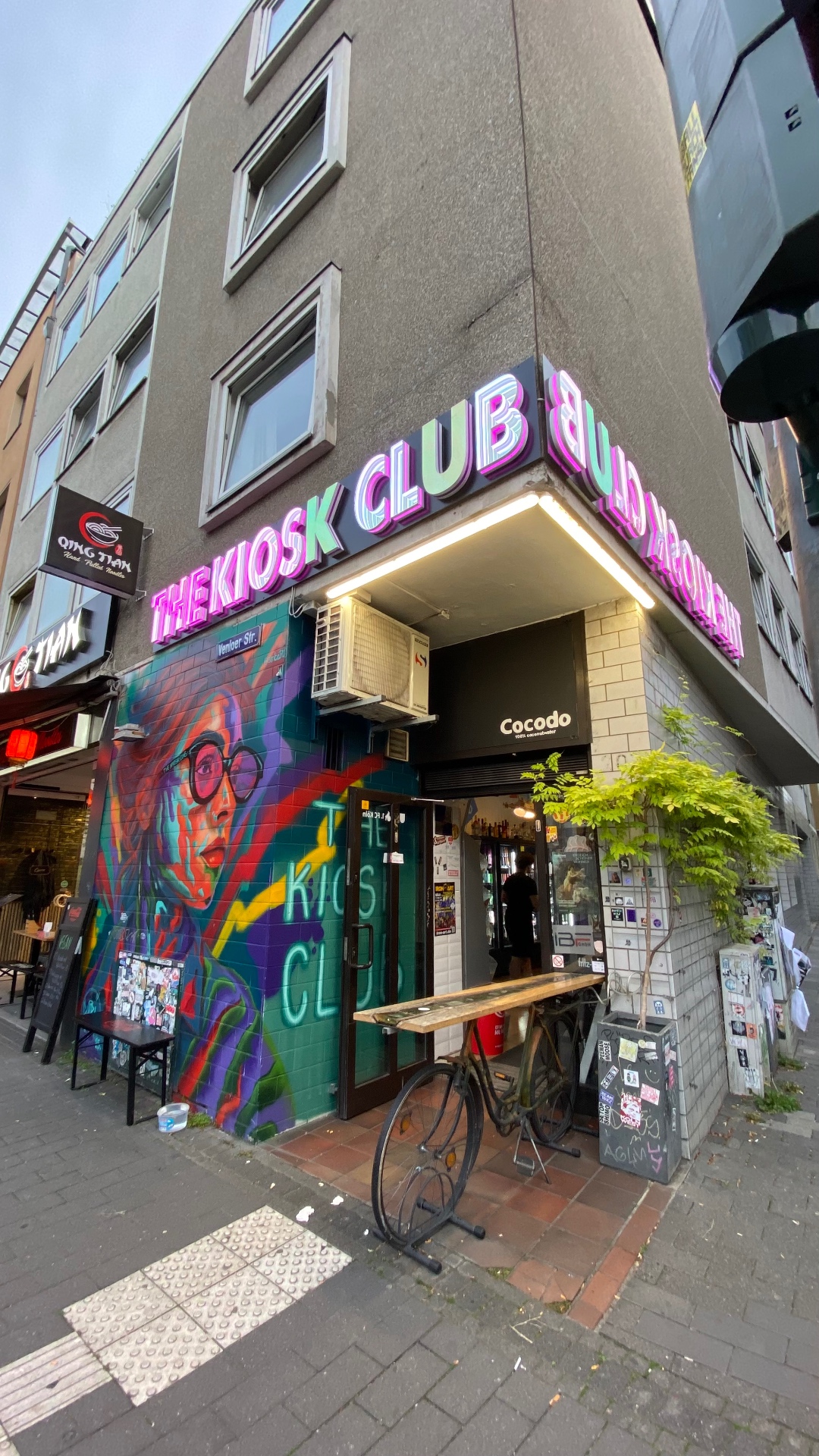 Außenansicht des The Kiosk Club mit Neon-Schriftzug und Street-Art-Fassade